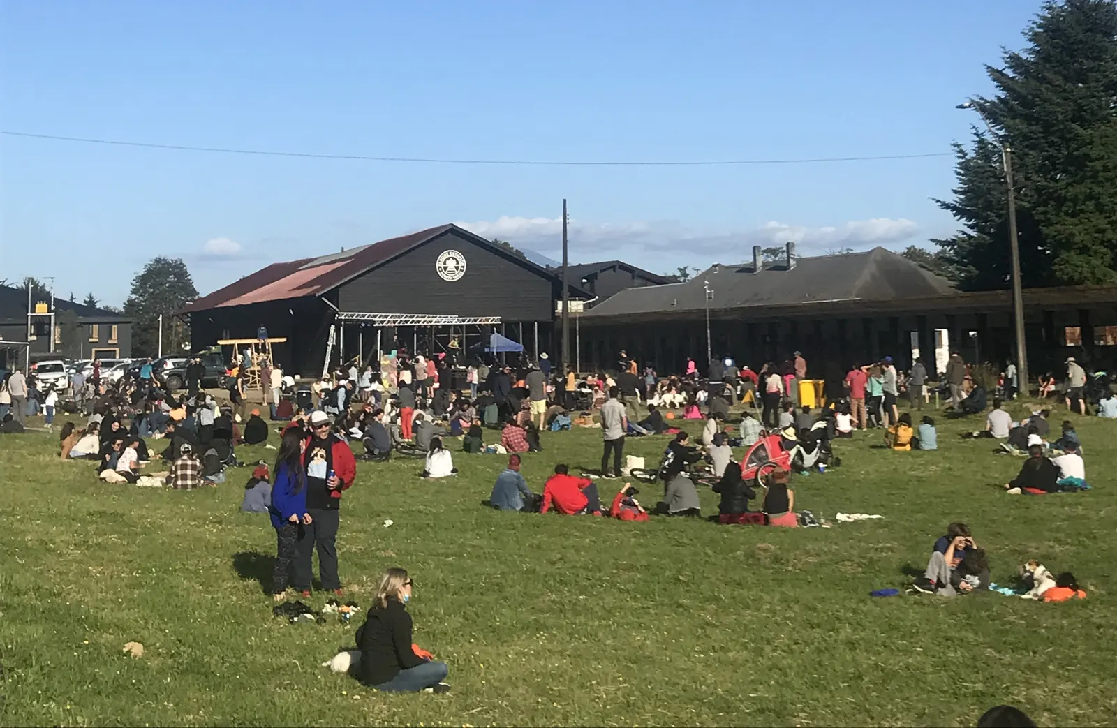 Cientos de personas sentadas en el pasto frente al Galpón Estación