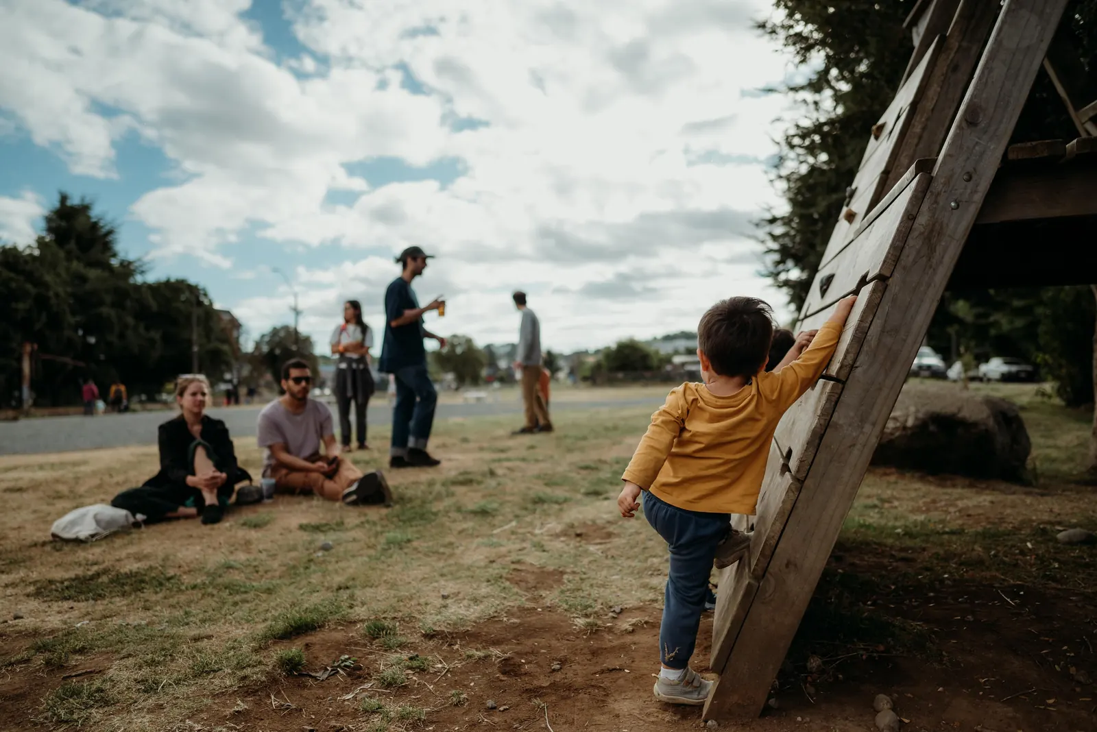 Niño trepando un juego de madera mientras familias descansan en el pasto