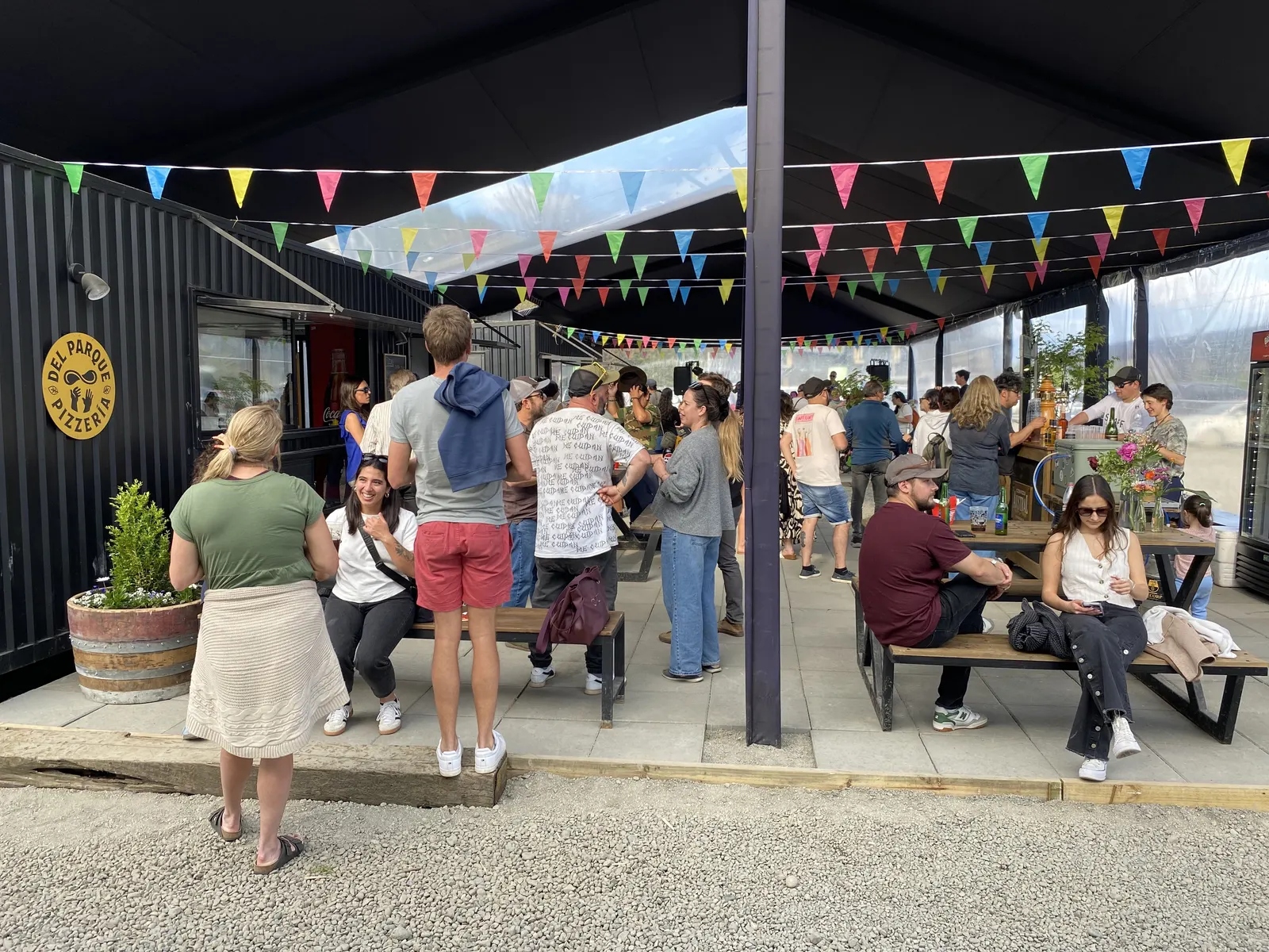 Carpa del Bloque Gastronómico con banderines, mesas y público junto a la Pizzería del Parque