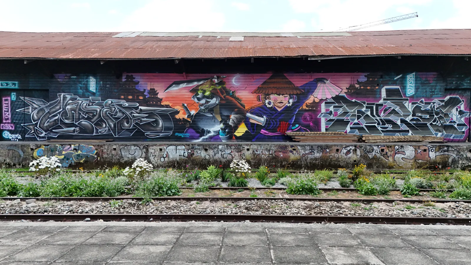 El corredor florecido frente al mural del Galpón Estación