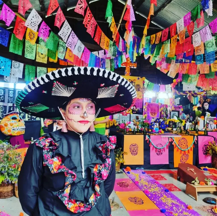 Persona caracterizada de catrina con sombrero de charro frente al altar
