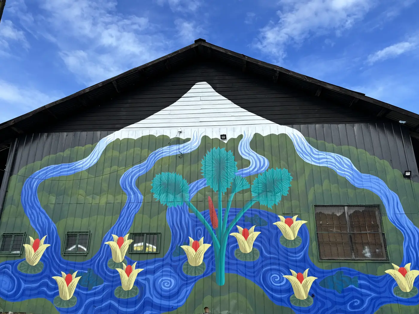 Mural de Michael Yaikel en el Galpón Estación: un volcán nevado, ríos azules, flores amarillas y un árbol turquesa